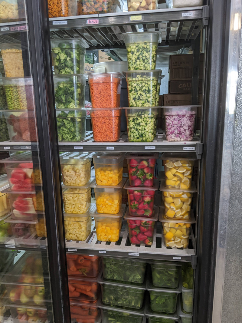 A refrigerated display case stocked with fresh, healthy to-go meals and snacks at All Good Eats & Drinks.